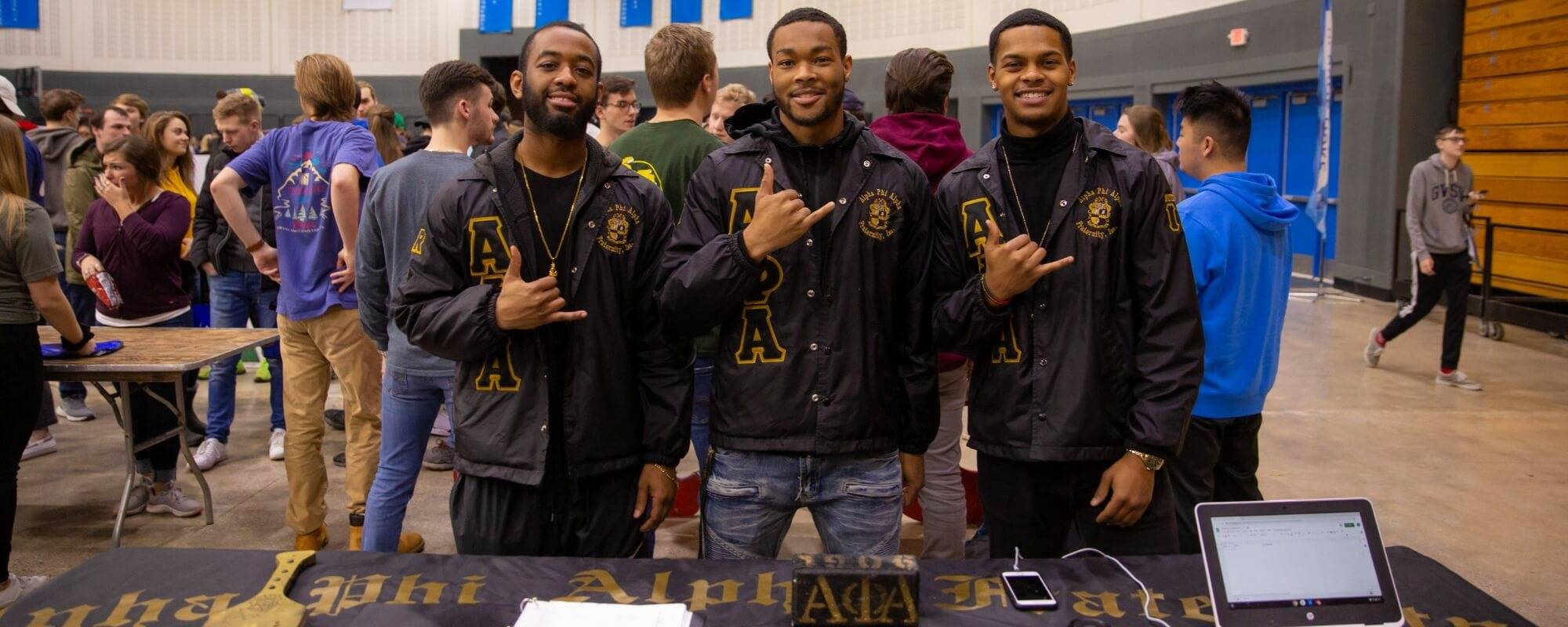 Three men in the Fieldhouse Arena tabling for their organization, Alpha Phi Alpha.